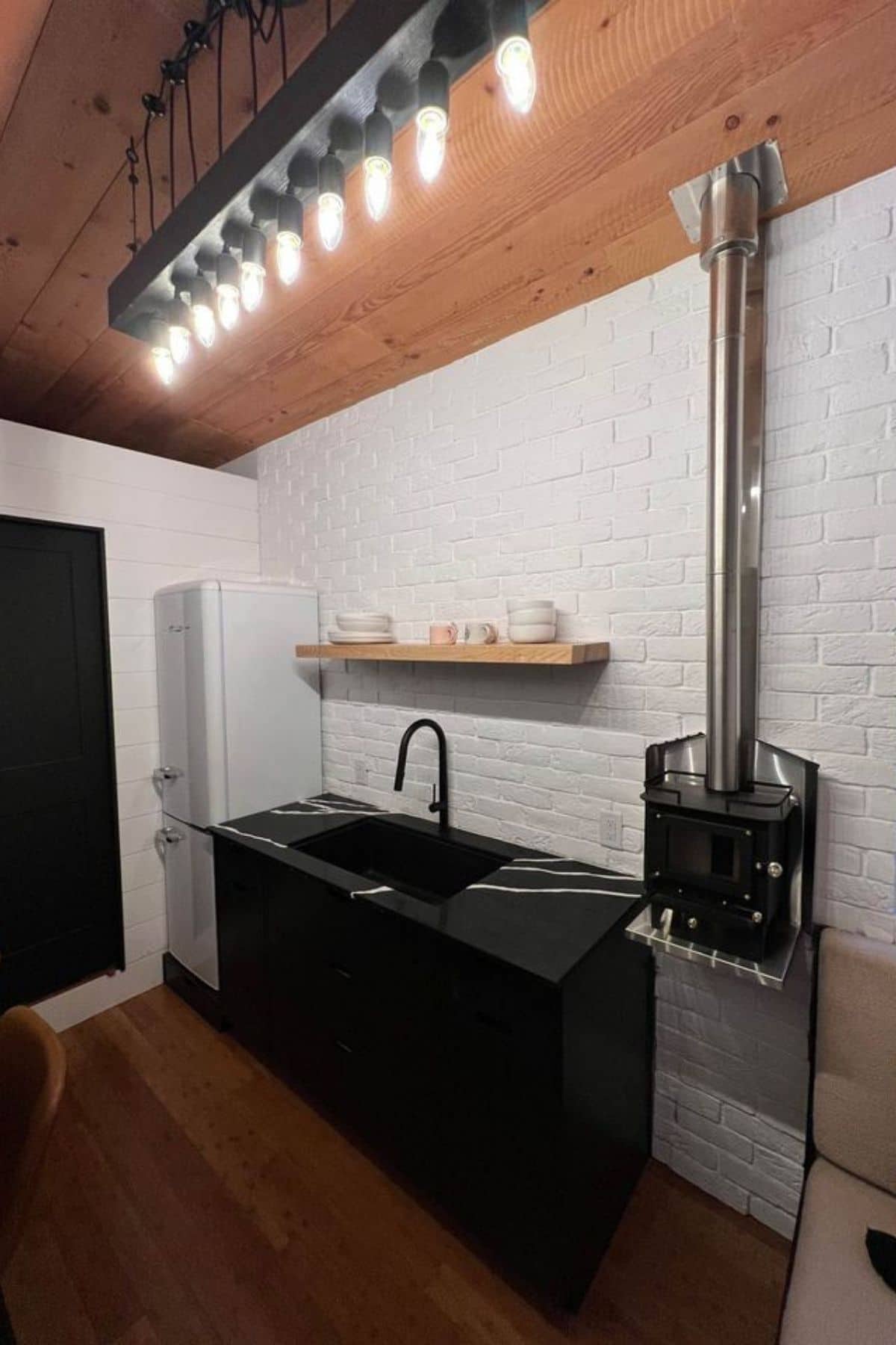 stove on wall next to black cabinets with sink in middle and wood shelf above