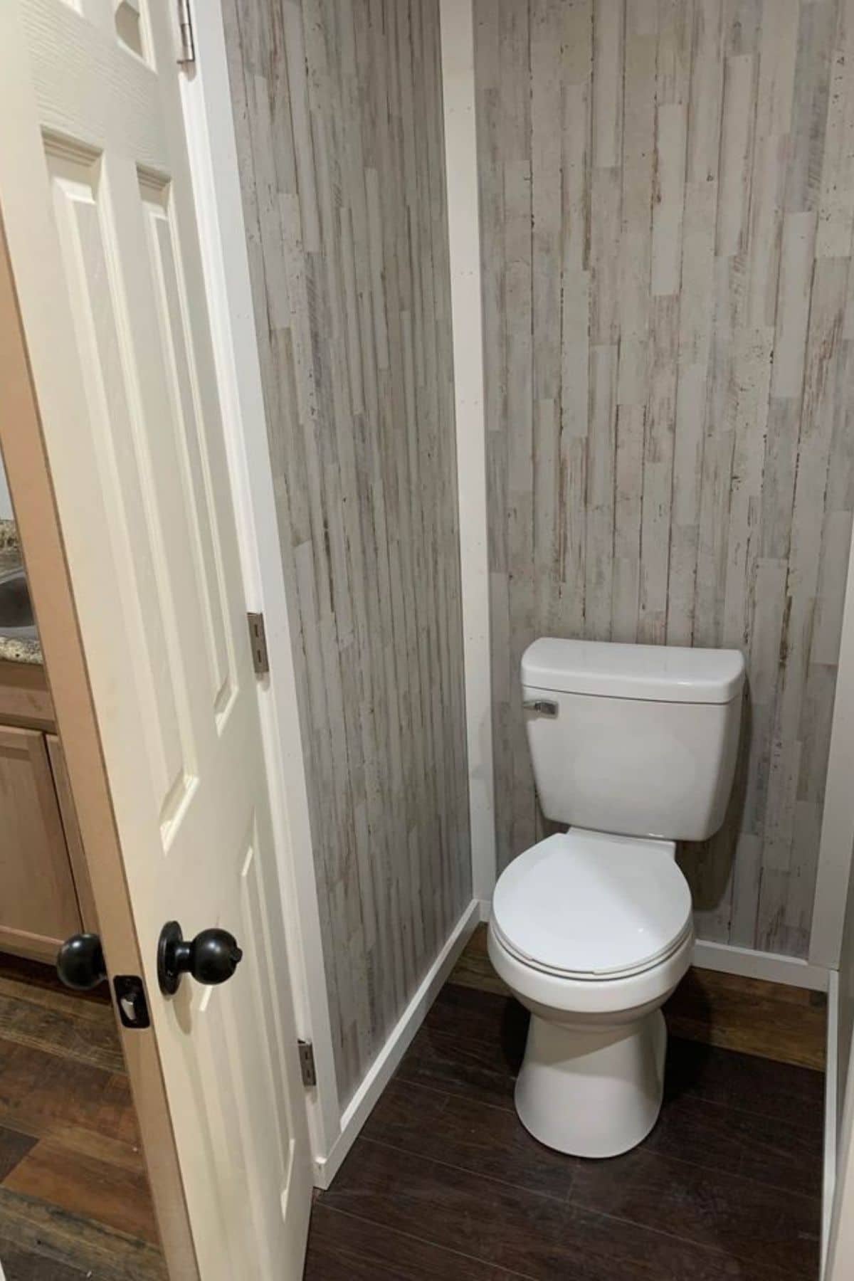 white flush toilet against light wood wall of tiny home bathroom