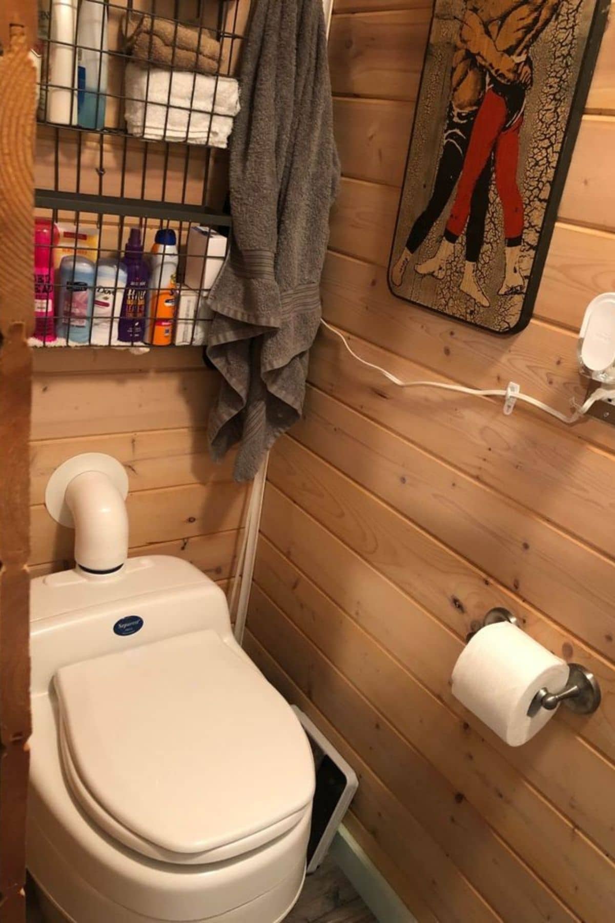wood walls in bathroom with composting toilet and wire shelf above toilet