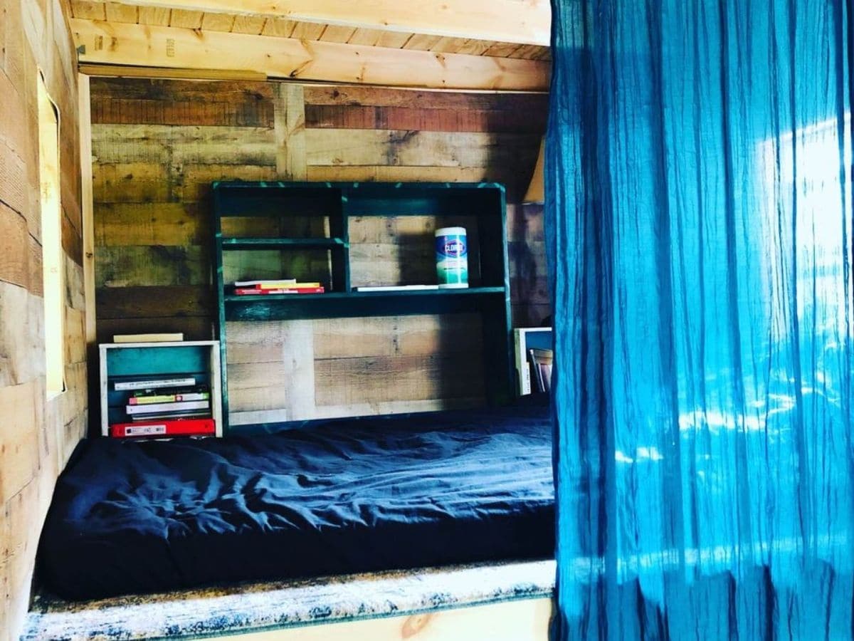 tiny home bedroom loft with black blankets and blue curtain in front