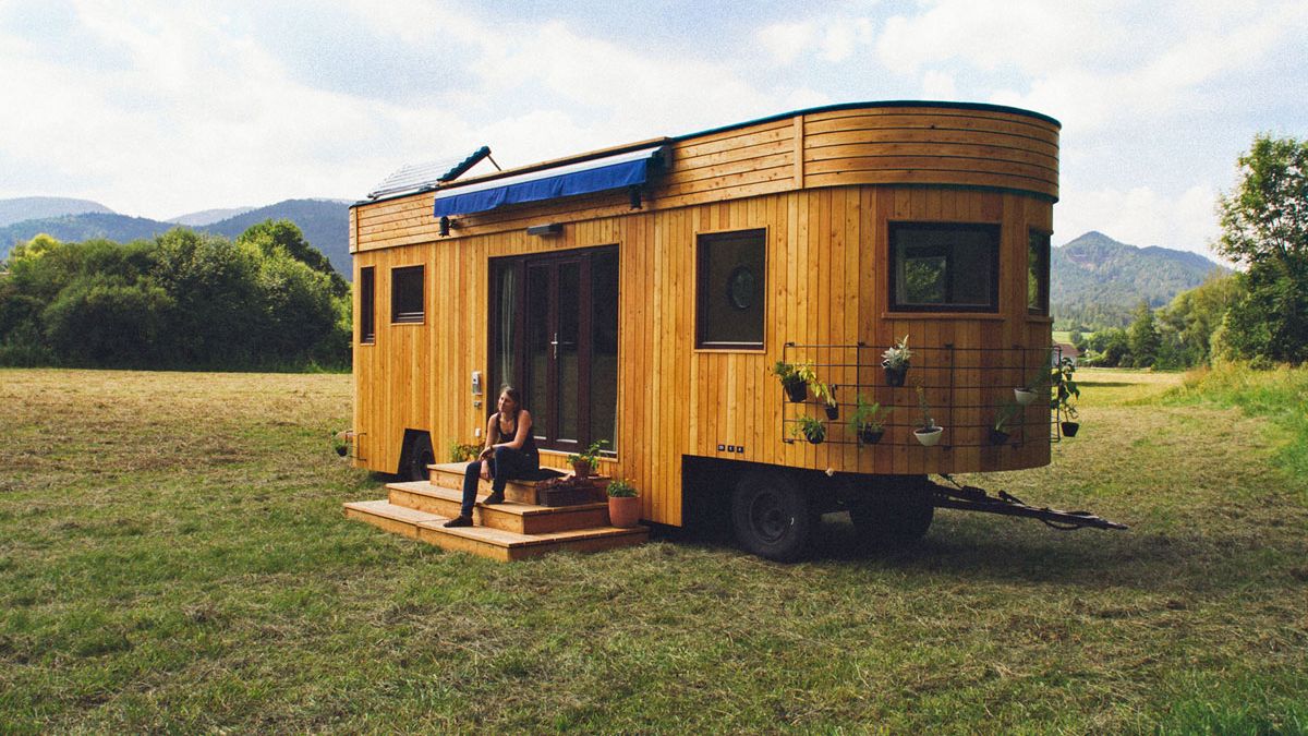 Woman sitting in front of the door of a rustic styled tiny house