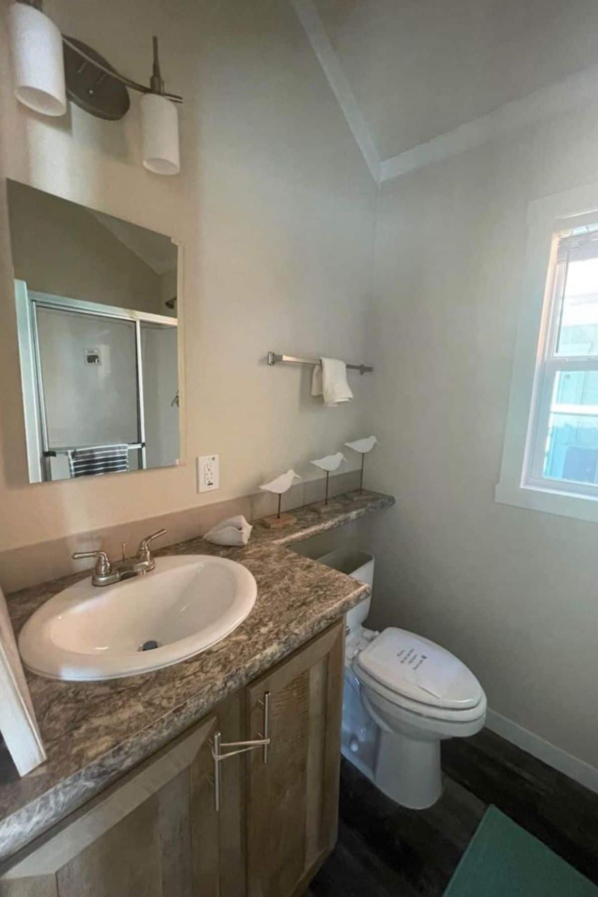 bathroom with wood cabinet under white sink with wall mirror and white toilet against wall by windw