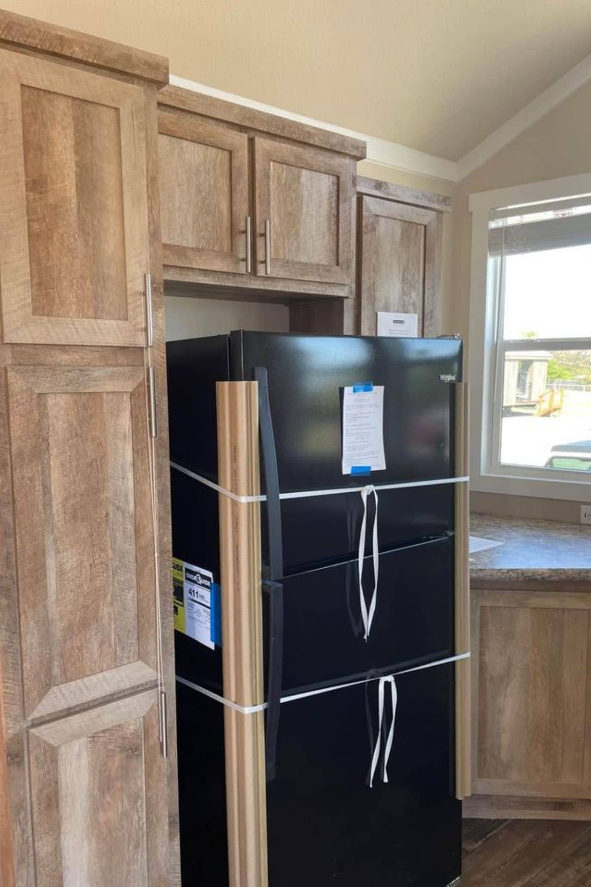 black refrigerator in between wood cabinets in kitchen