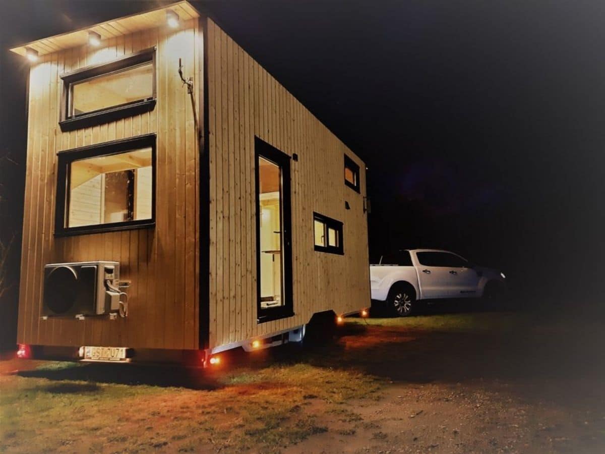 light wood tiny house with black trim pulled behind white truck