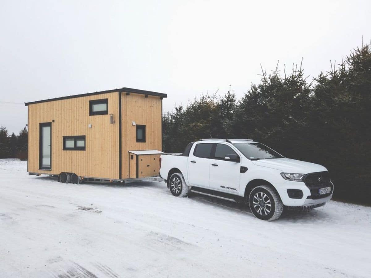 light wood tiny home behind white truck on snow