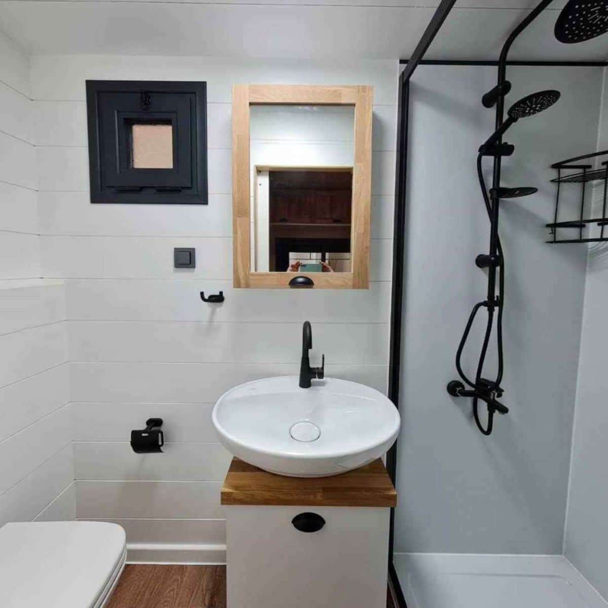 white walls with white cabinet and white bowl sink next to open shower with black fixtures in bathroom