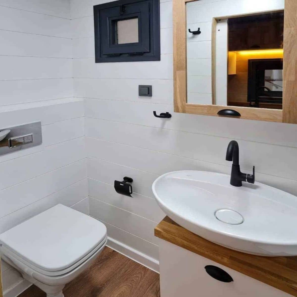 square toilet seat against white wall with white bowl sink under mirror with wood frame