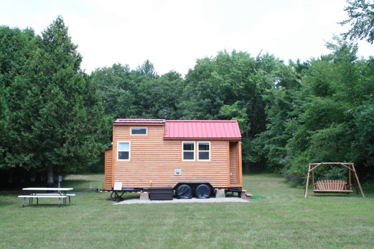 tiny home parked on concrete with red roof and wood siding