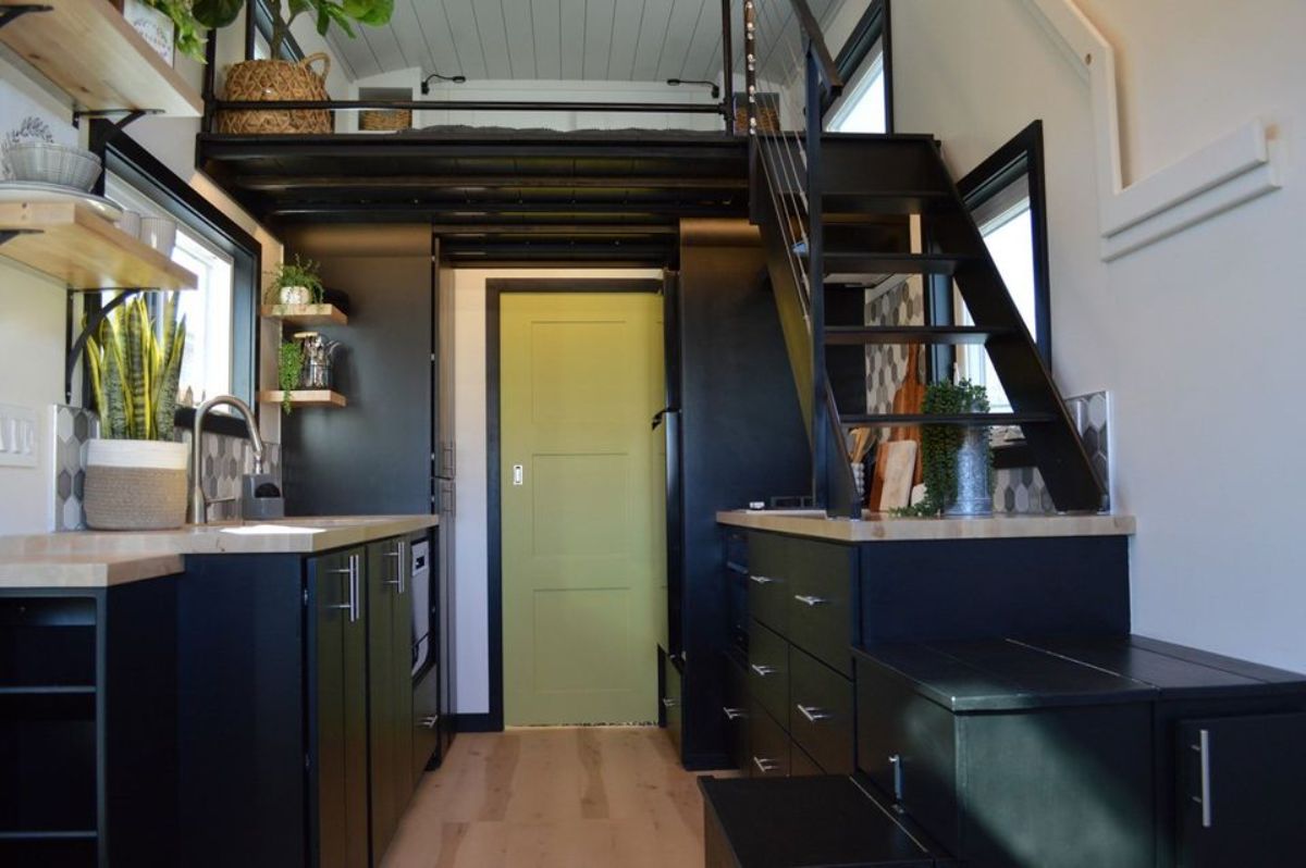 black cabinets and trim inside tiny home kitchen with green door at back of space