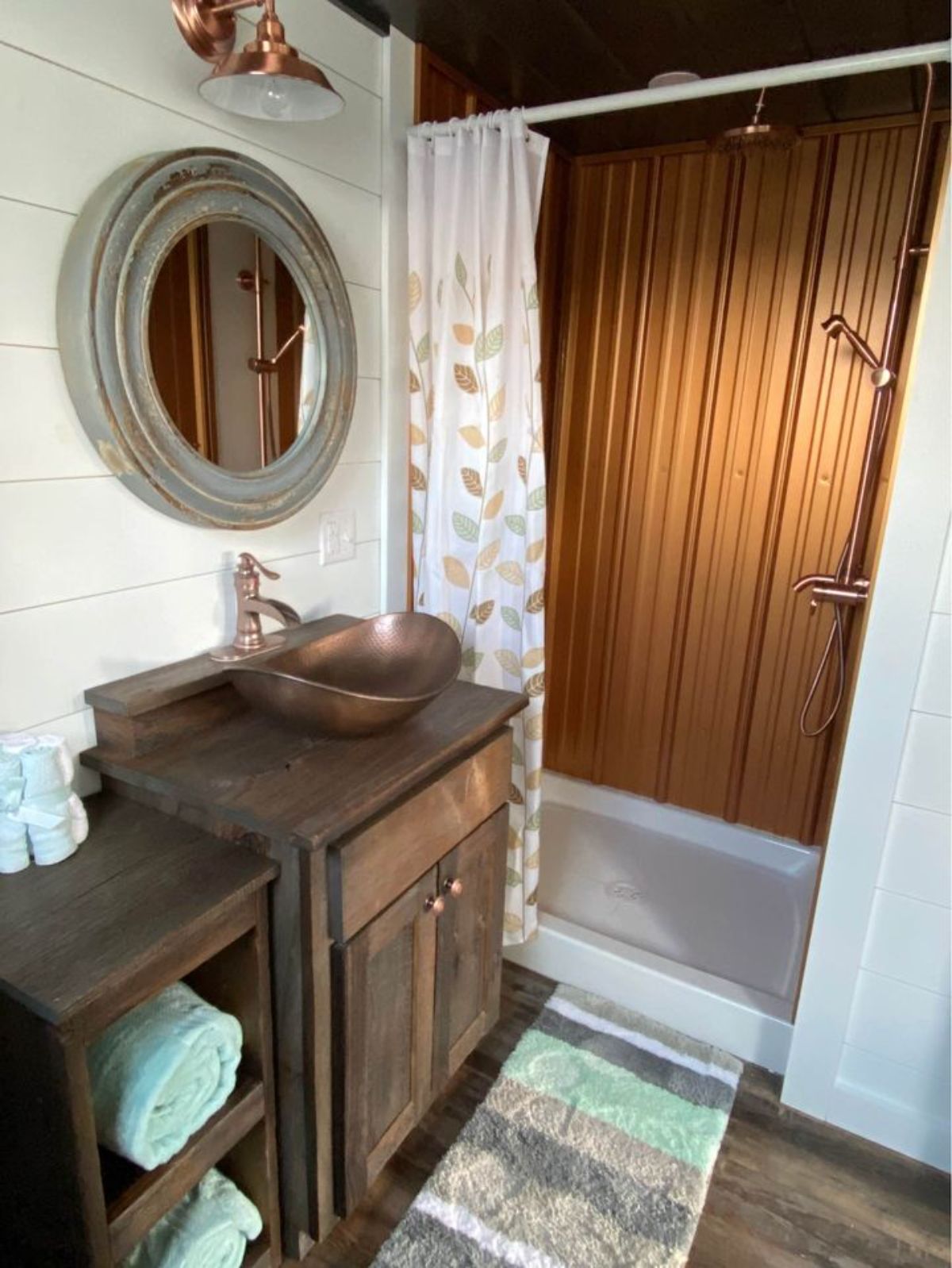 dark wood vanity with copper sink next to shower with copper shower wall and white bottom