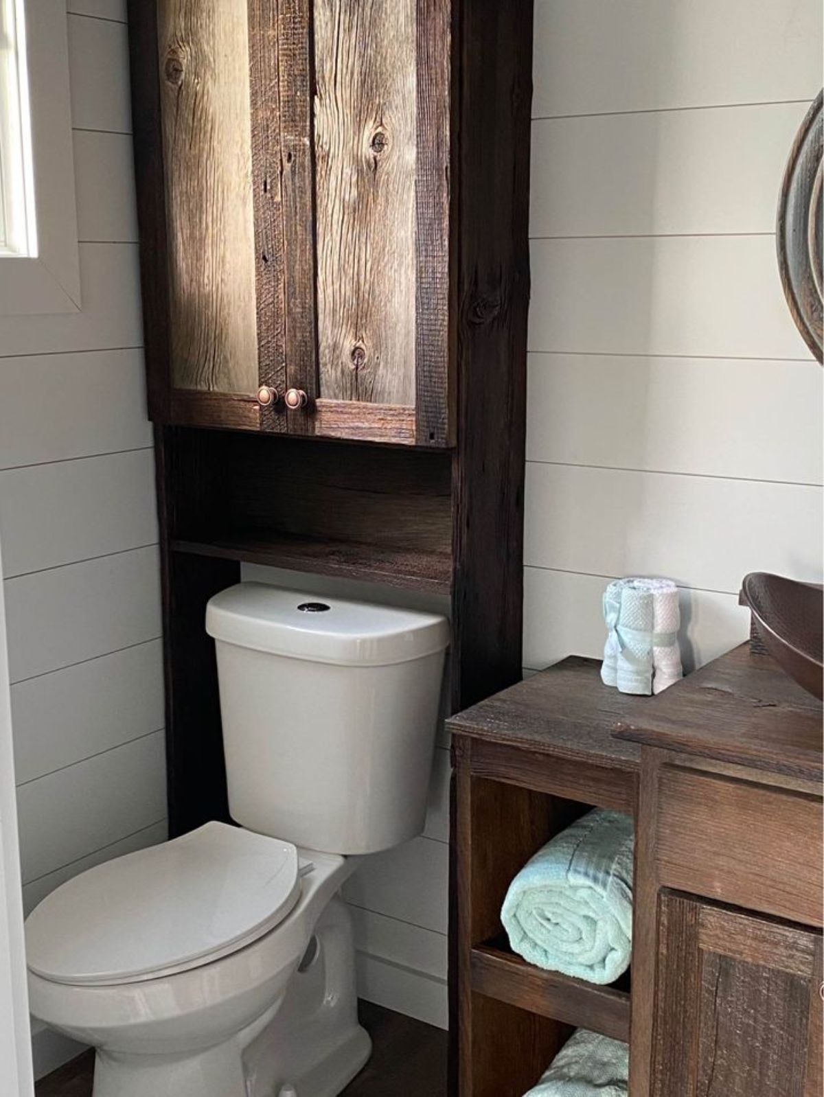 white flush toilet against wall under dark wood over toilet storage cabinet