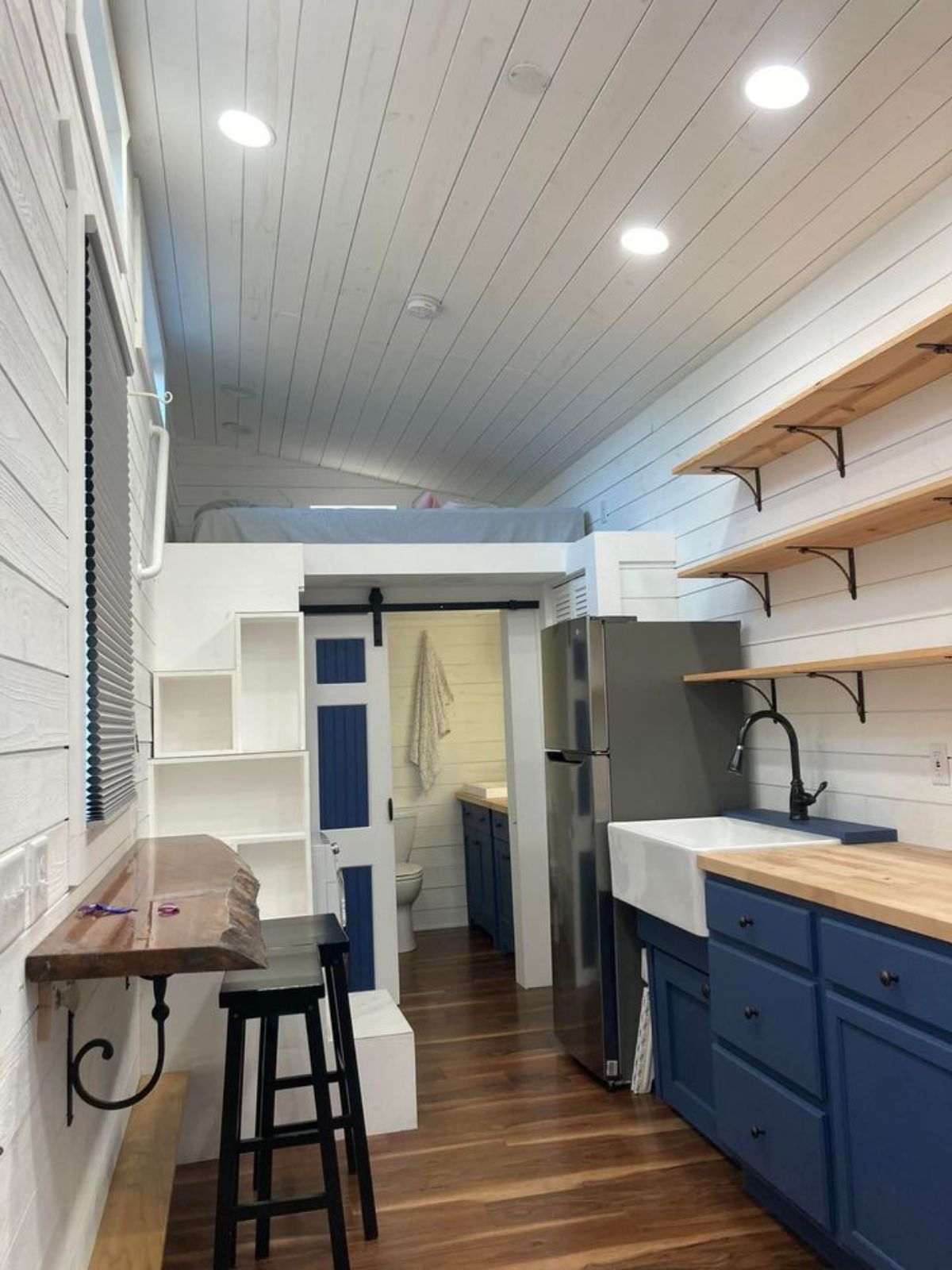 shelf below window on right and blue cabinets with butcher block counters on right of tiny home