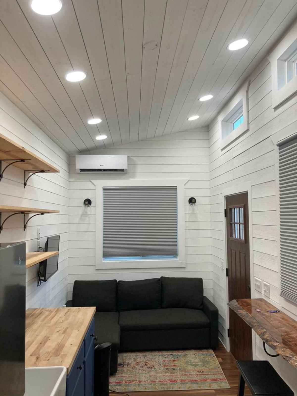 white shiplap walls inside tiny house with black sofa against back wall