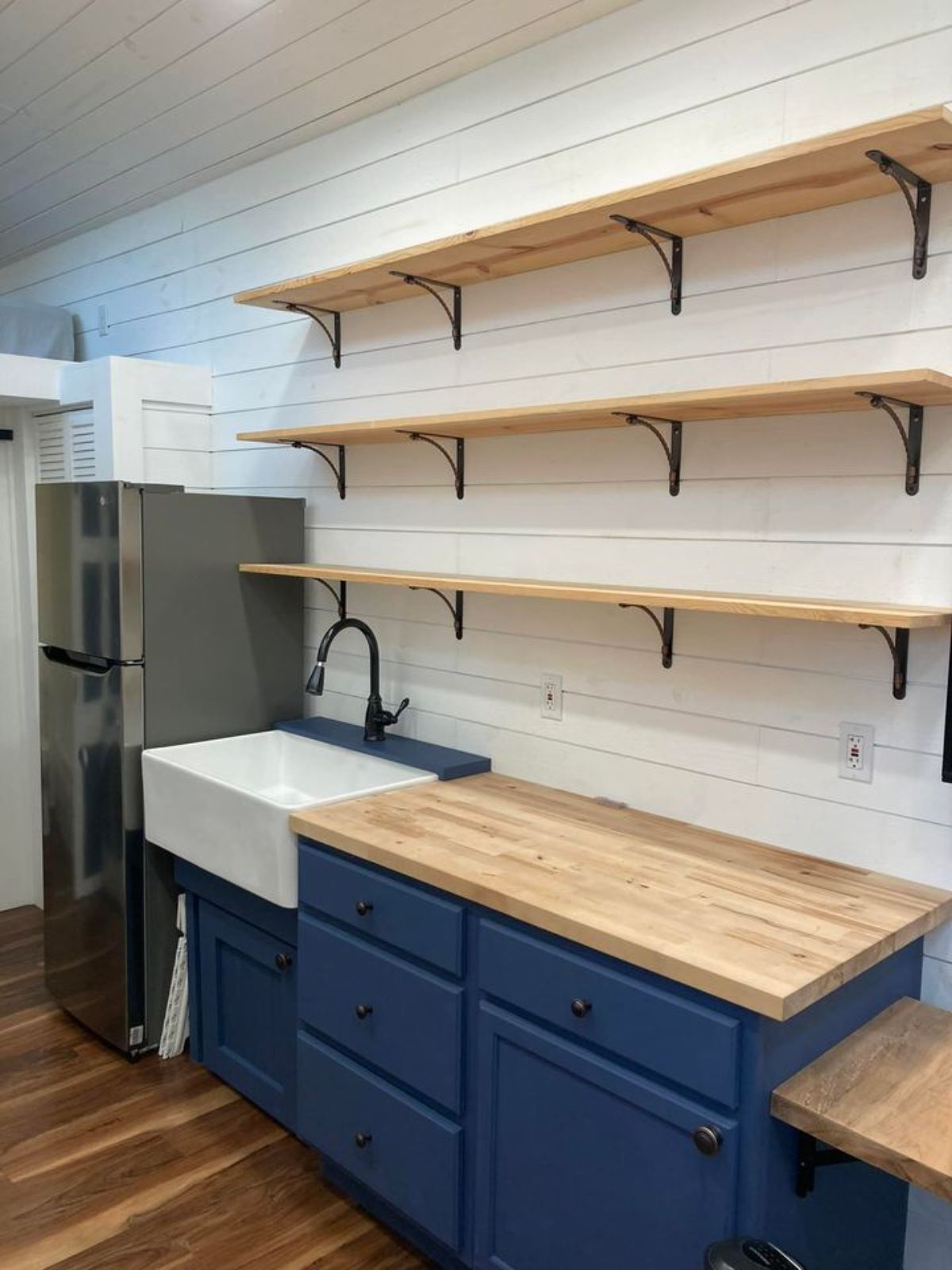 blue cabinets beneath butcher block countertop with white shelves on wall