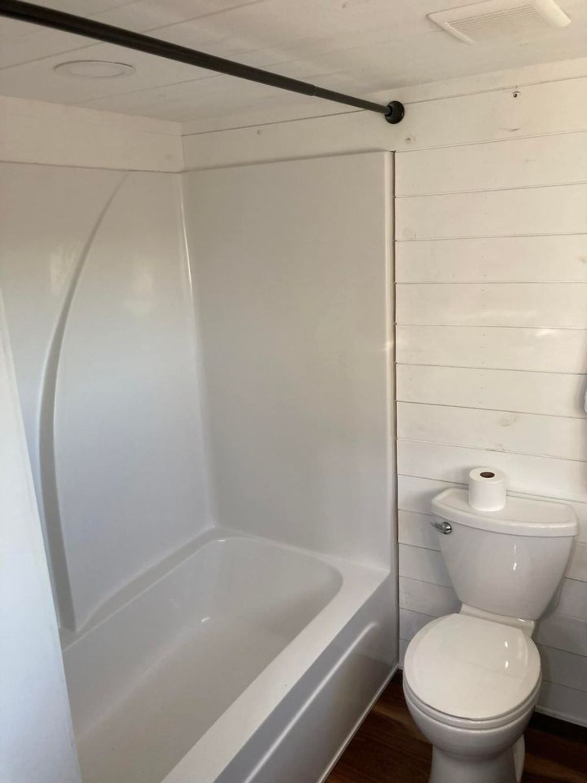 white shower in bathroom with white flush toilet and white shiplap walls