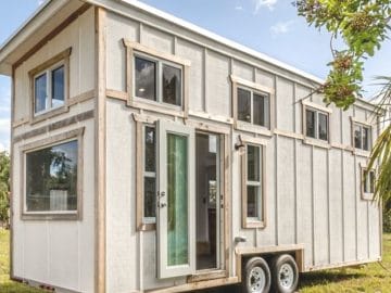 white tiny home with wood trim and windows along top half on green field