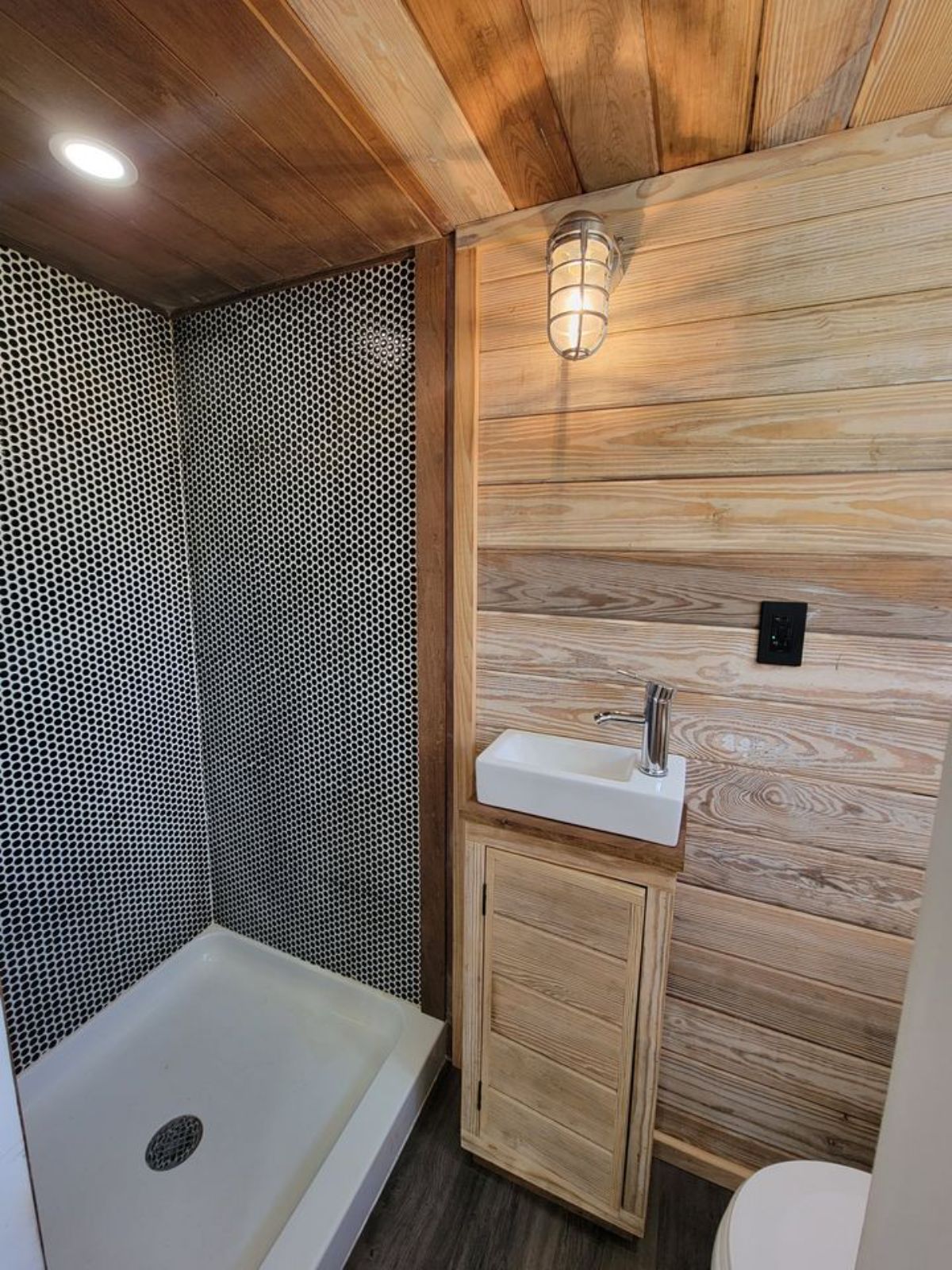 black and white tiled shower with white shower basin and wood walls