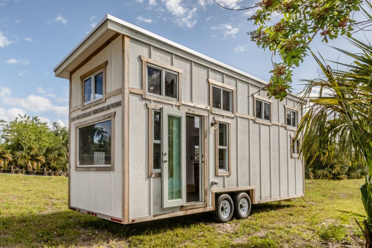 white tiny home with wood trim and windows along top half on green field