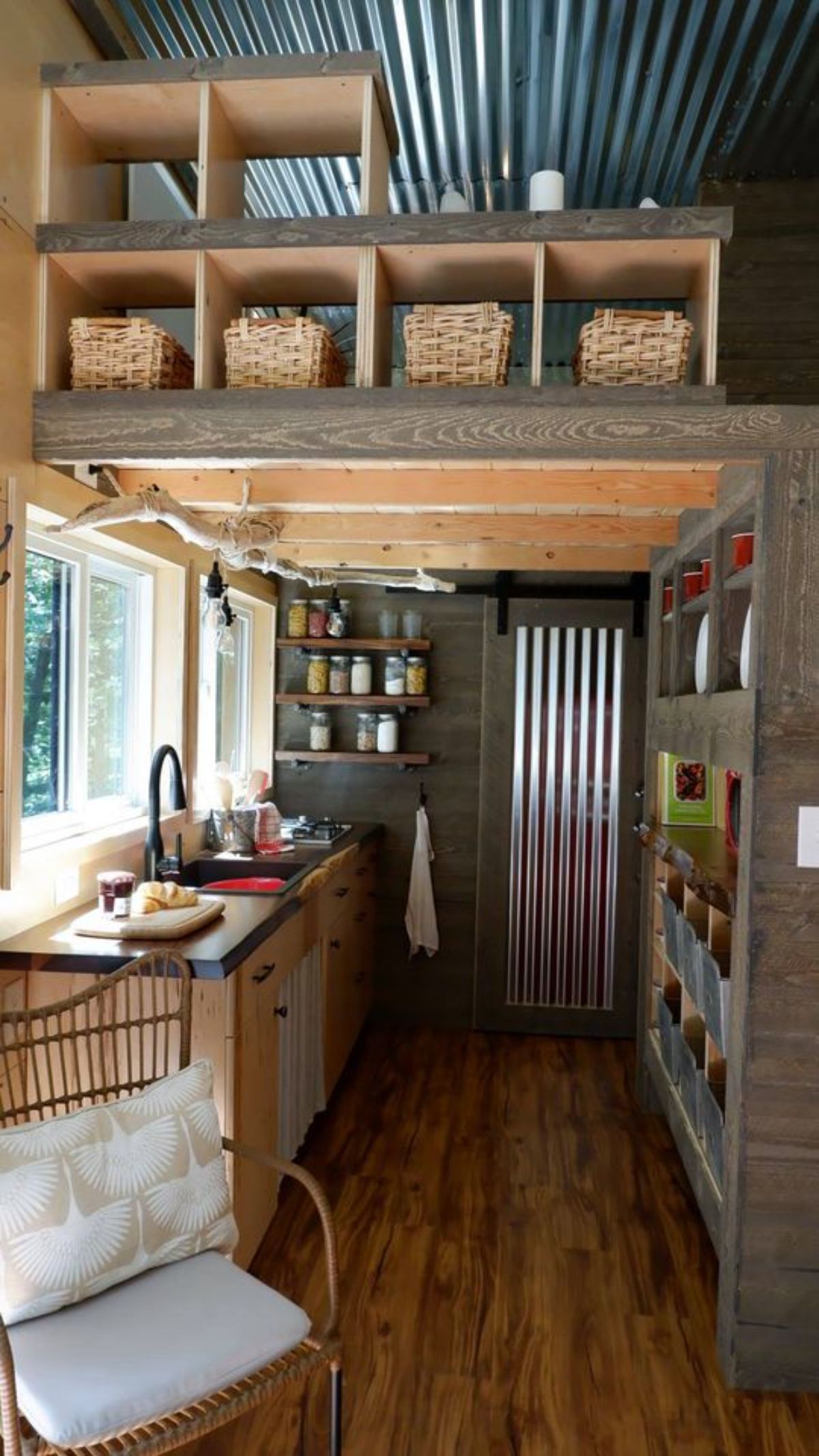 kitchen of tiny home with corrugated metal door at back and wall of storage on right
