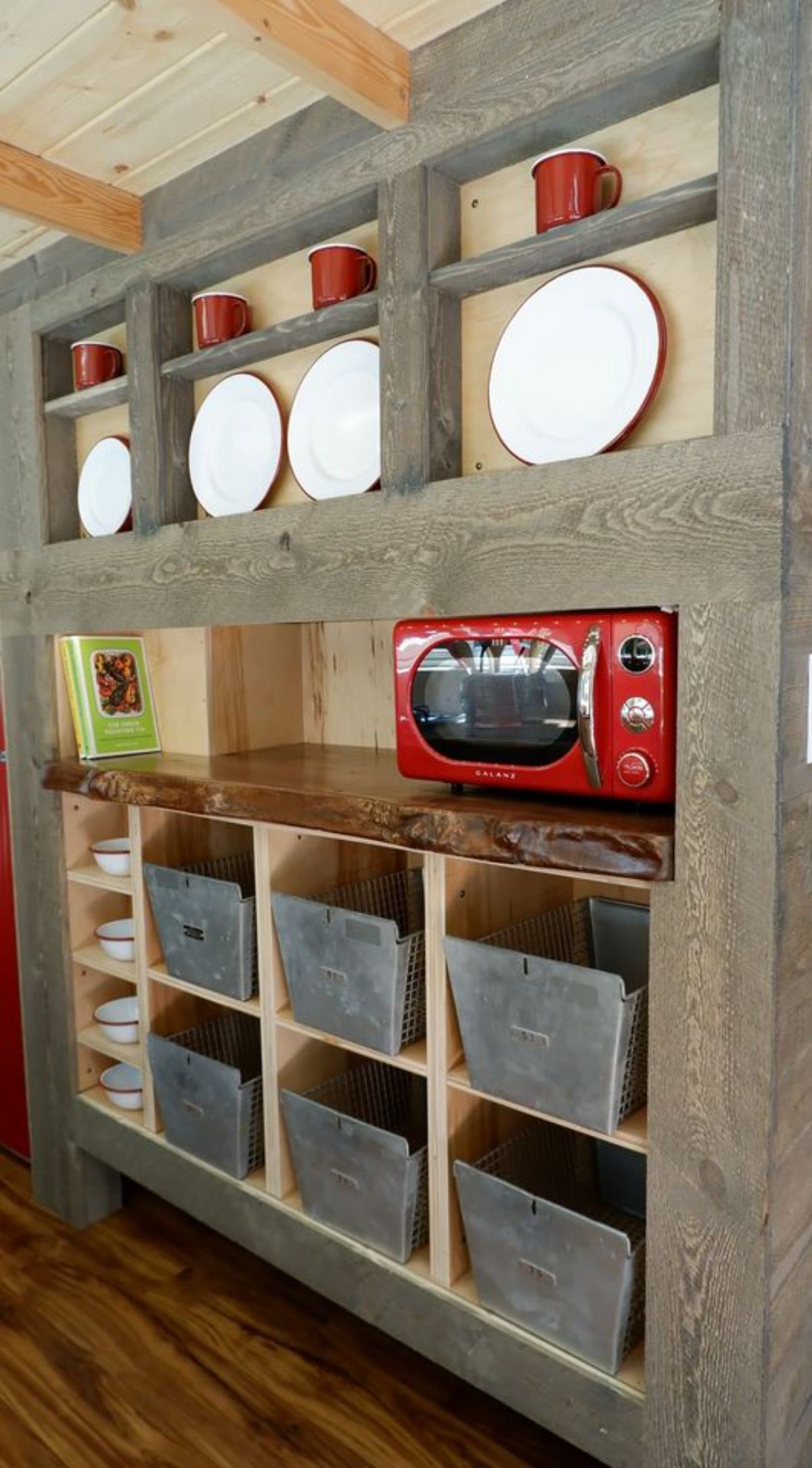 wood wall of cubbies with gray baskets and red microwave on middle open shelf