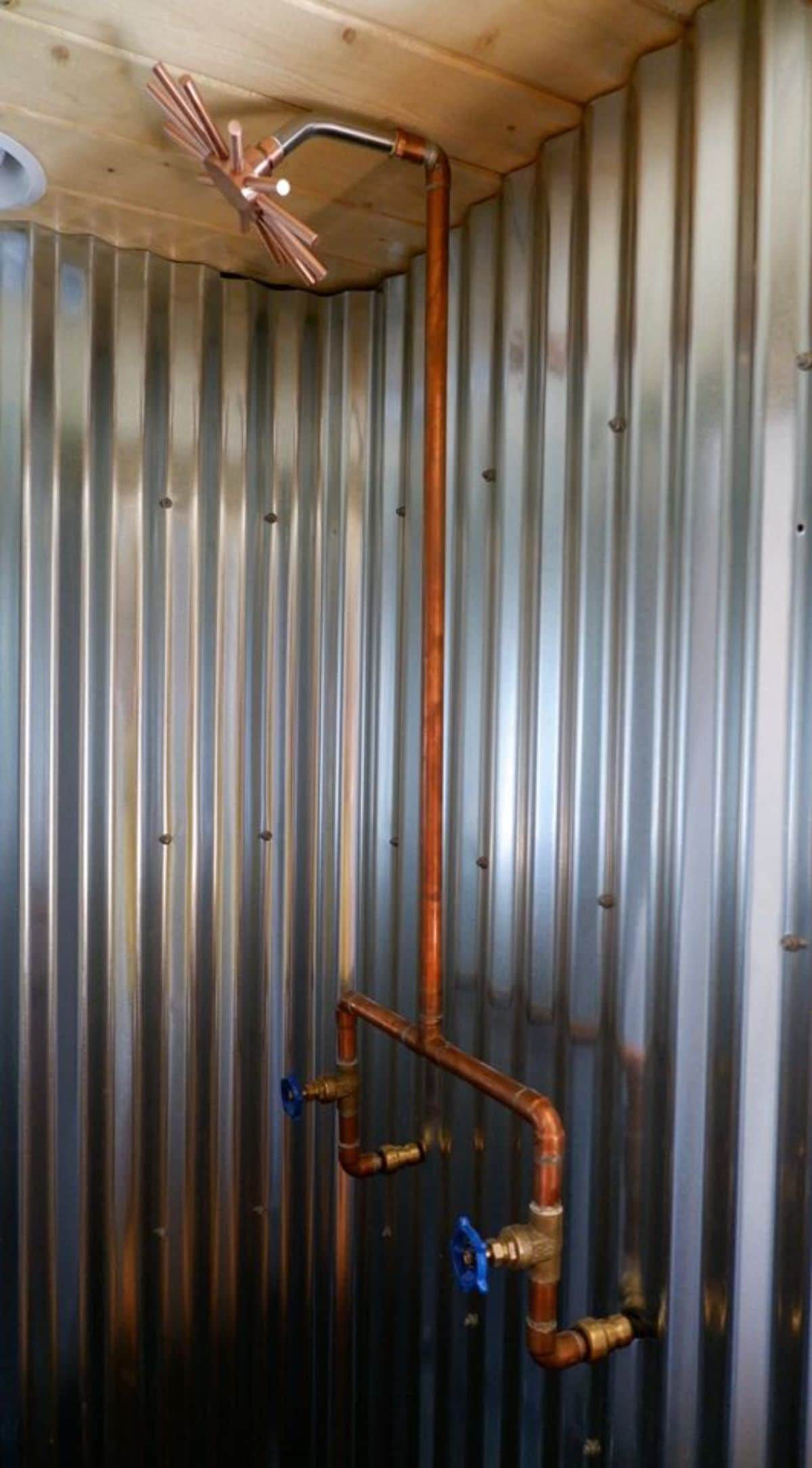 corrugated metal shower stall with brass pipes exposed