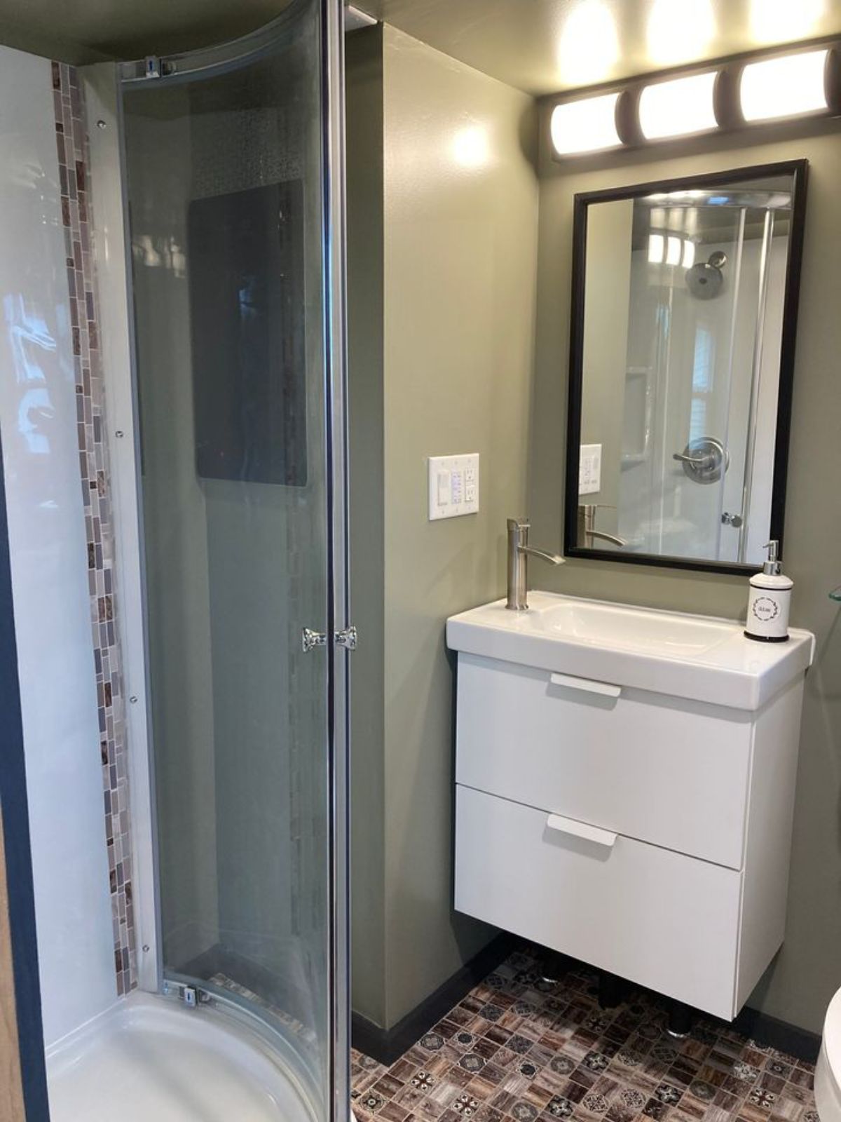 glass shower door to left of white wall mounted vanity beneath mirror