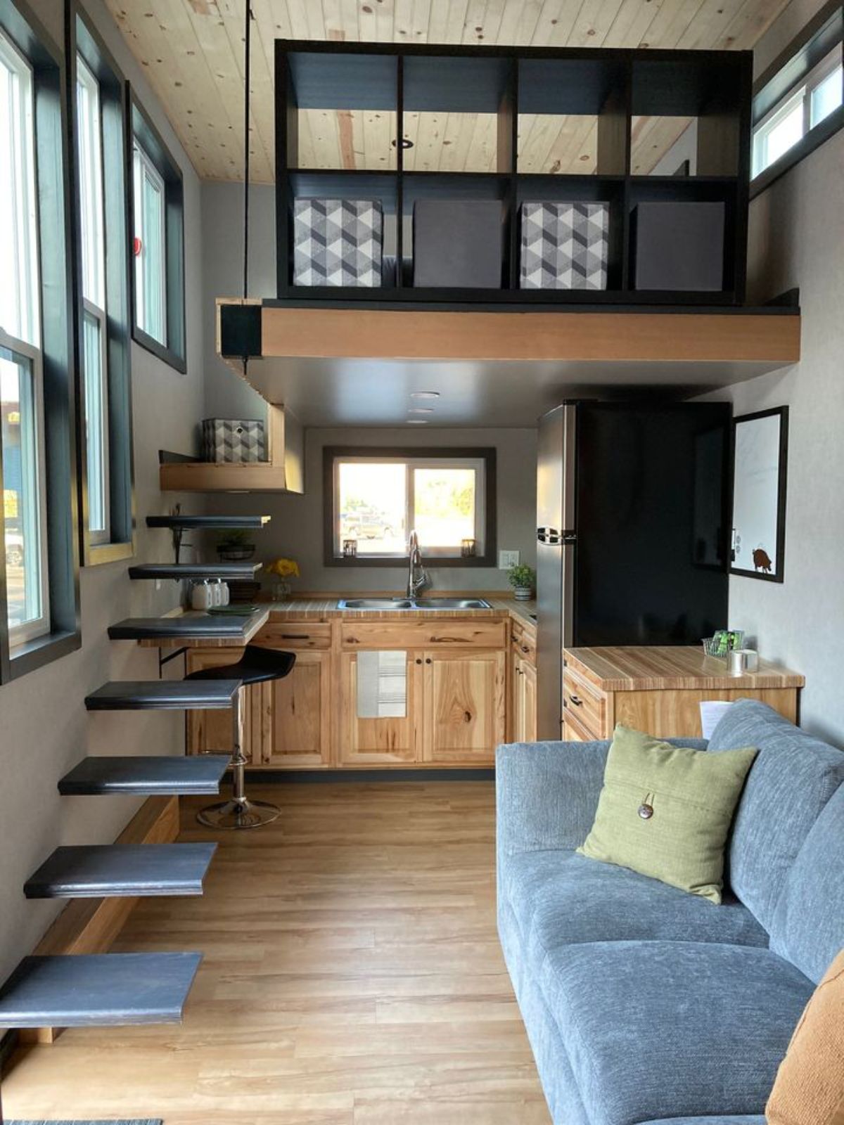 light gray sofa on right with floating stairs on left inside tiny home
