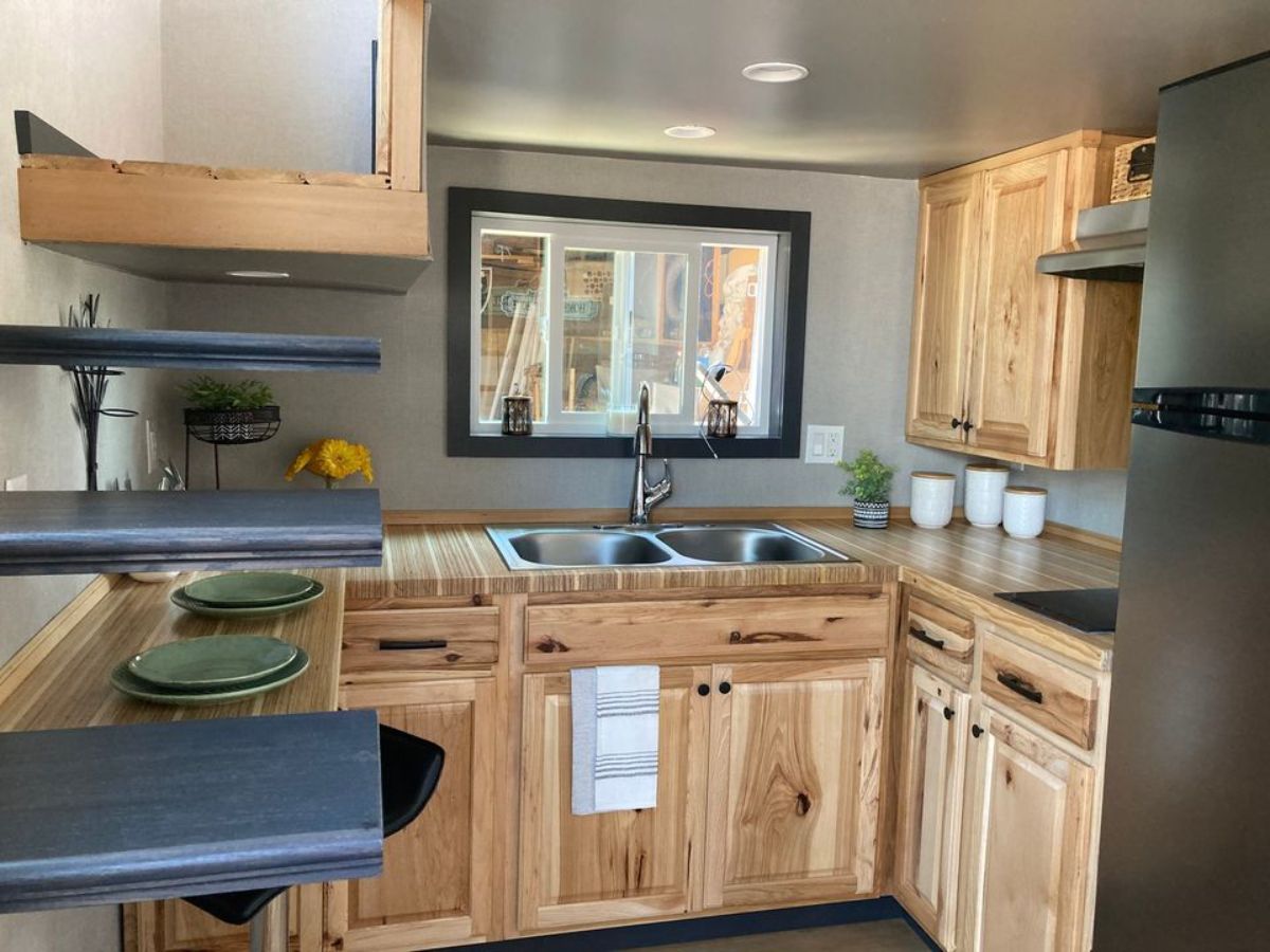 light wood cabinets in corner kitchen of tiny home with window on back wall
