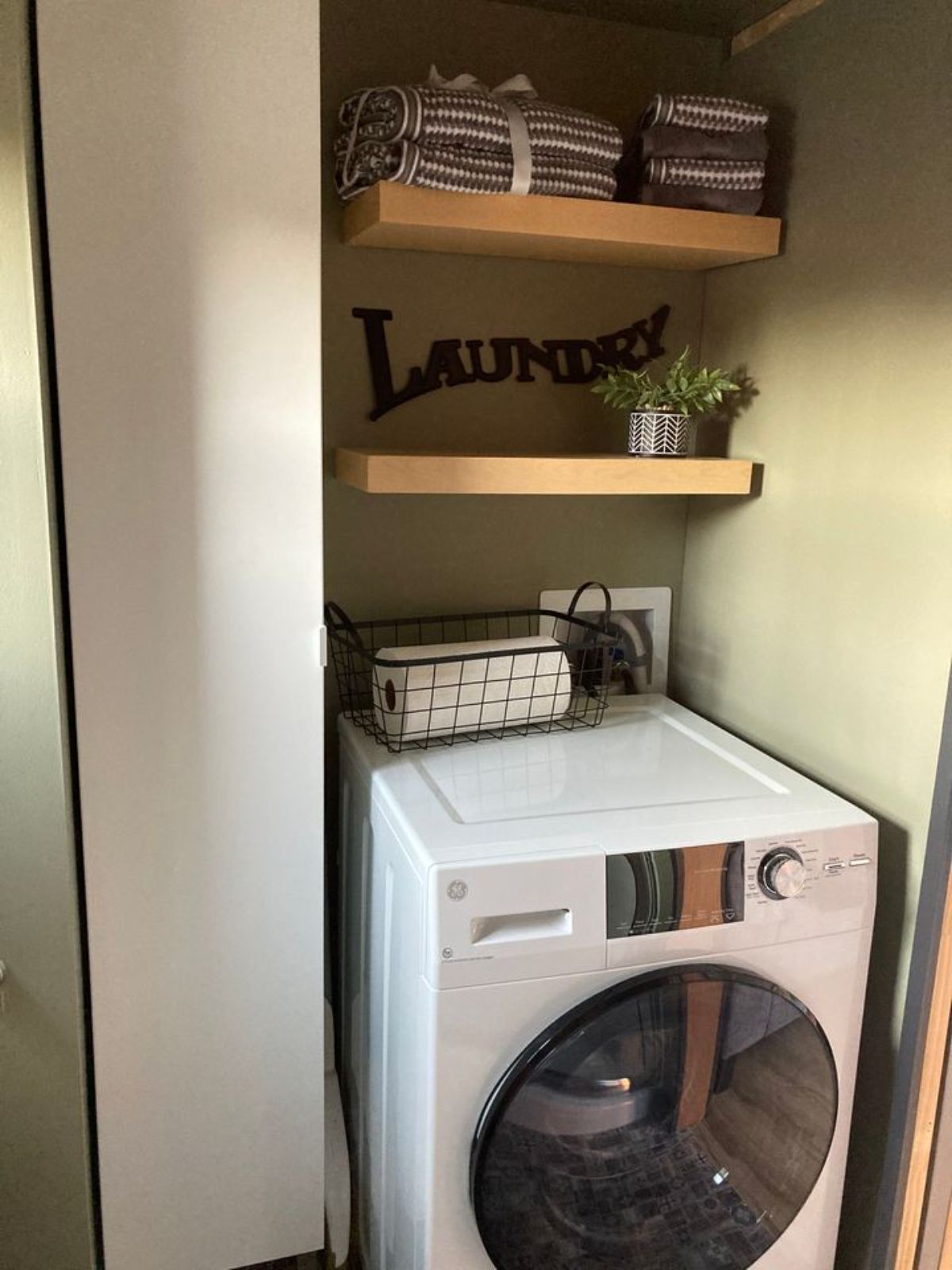 white combination washer and dryer beneath floating shelves above