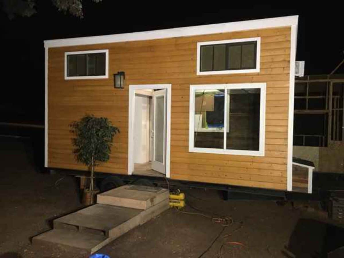 light brown tiny home front door open with white trim and small shrub by door