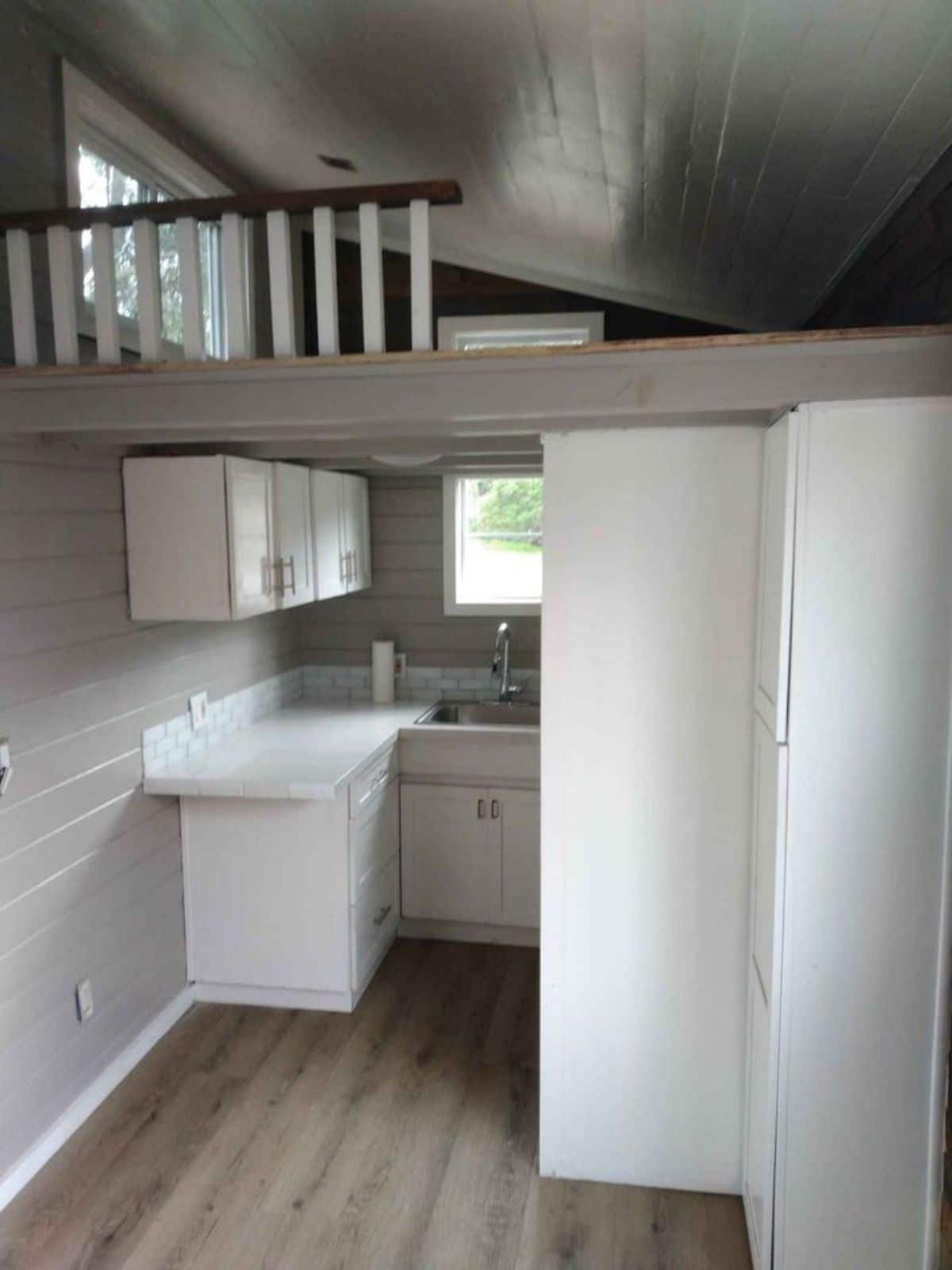 view into kitchen of tiny home with white cabinets and loft above