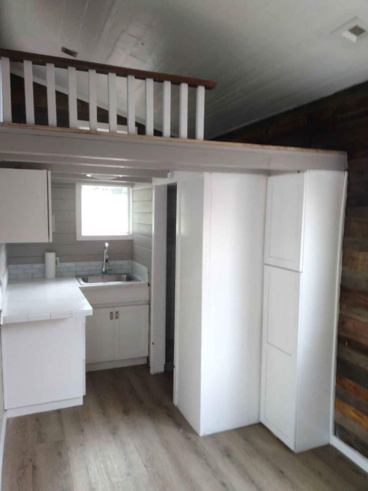 white pantry cabinets against reclaimed wood wall underneath loft with white railing