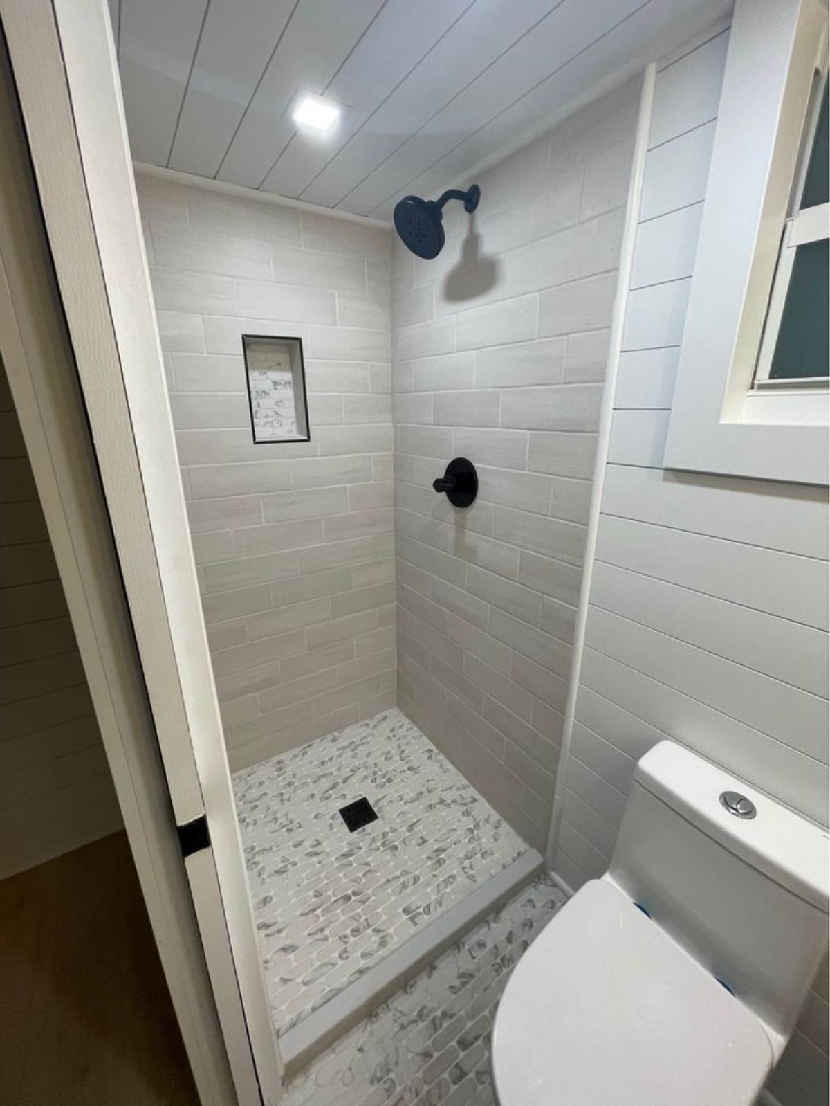 tiled shower stall next to flush toilet with black matte faucet and showerhead