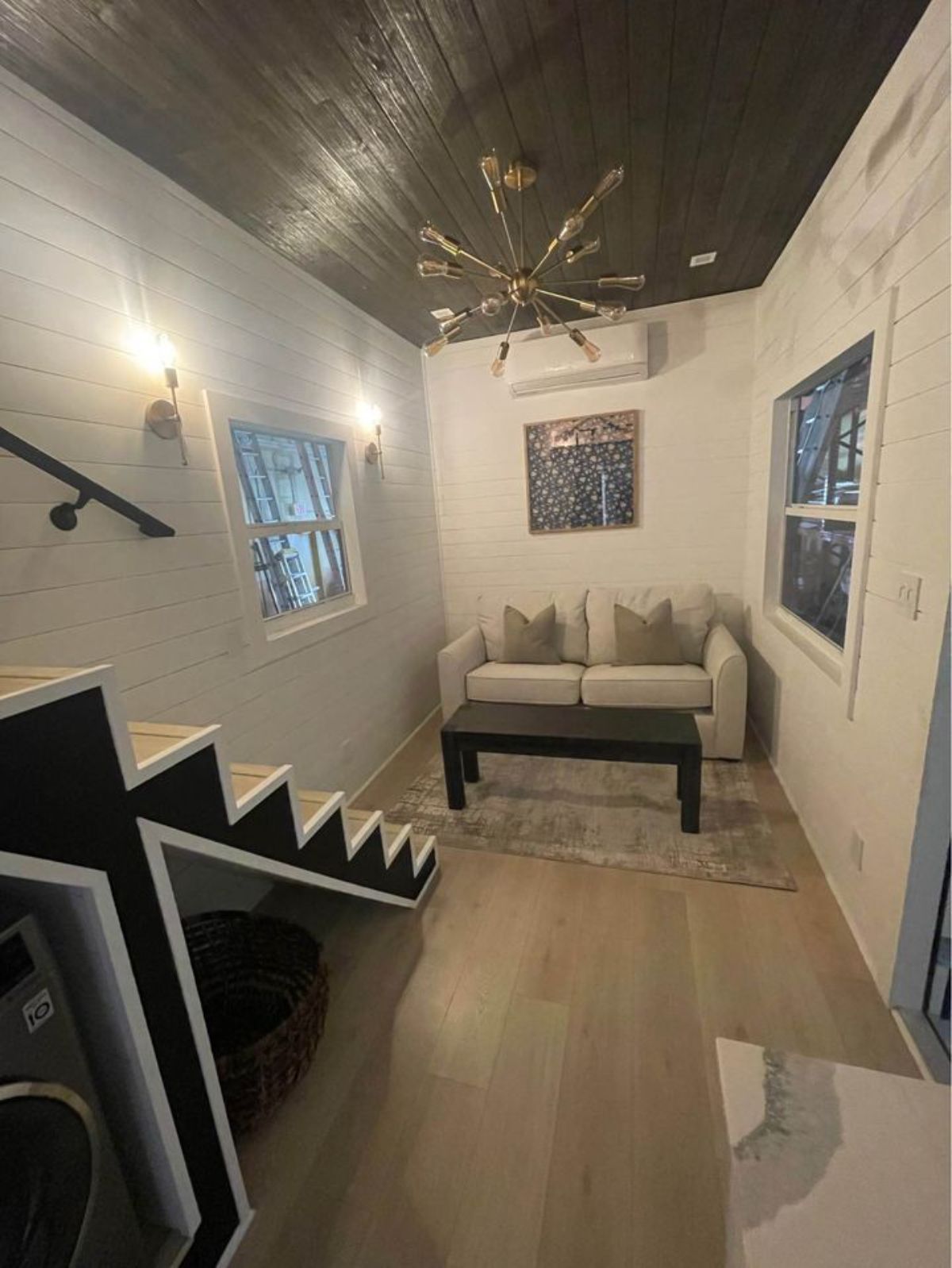 view from kitchen into tiny home living space showing windows on both sides and sofa against far wall
