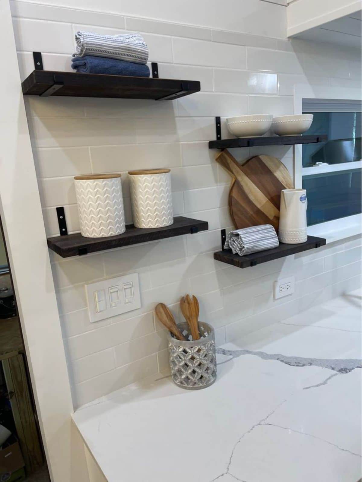dark wood floating shelves against shiplap wall above white marble kitchen countertop