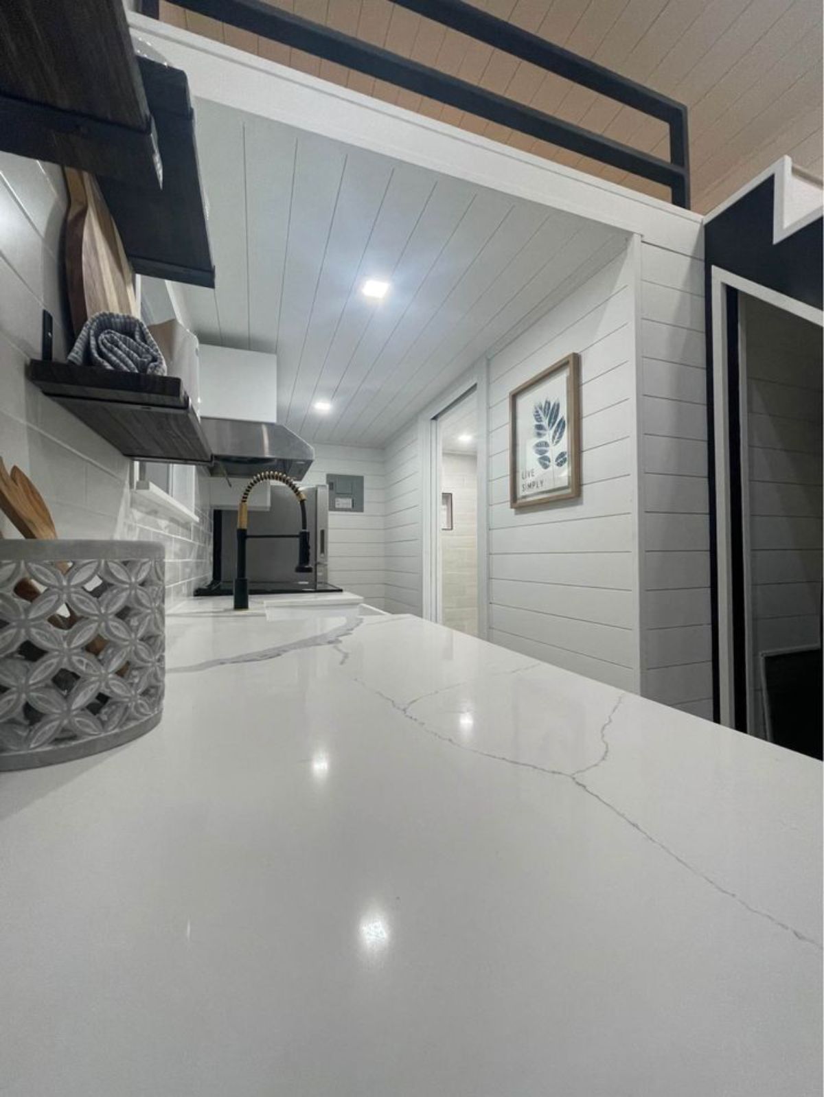 view across white marble counter in kitchen of tiny home showing open door to bathroom on right