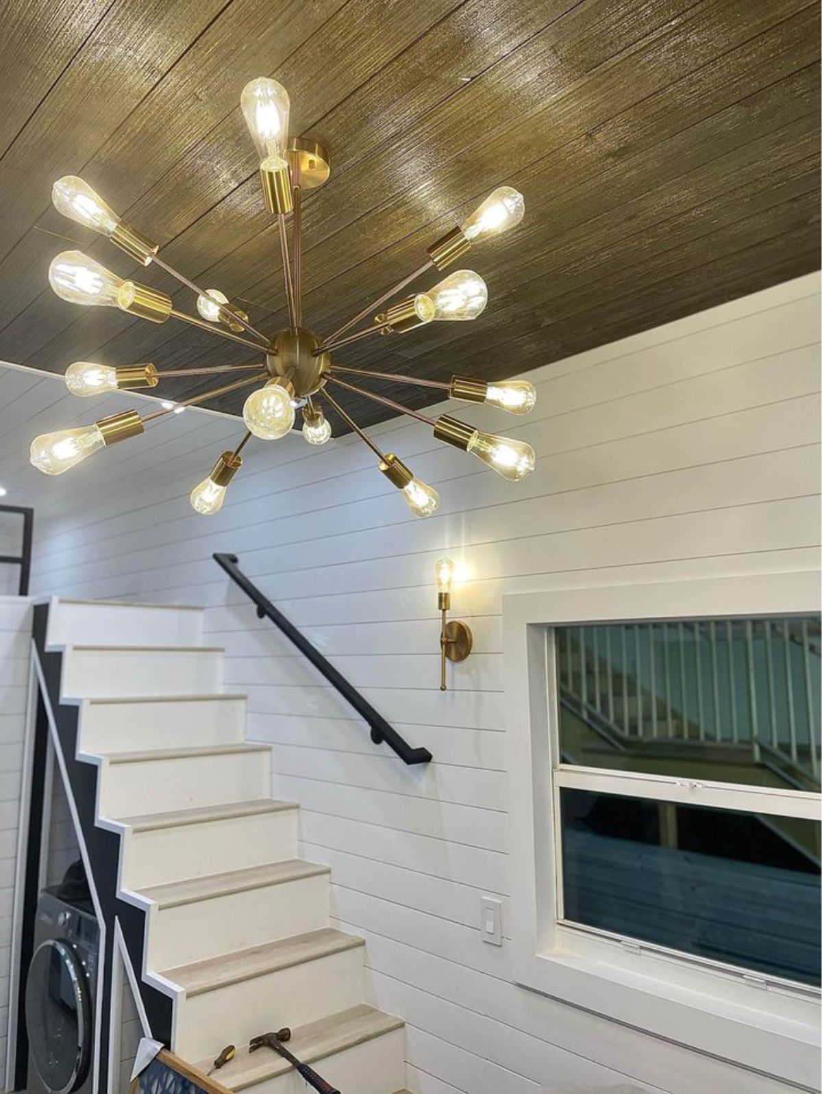 edison bulb starburst light fixture in middle of living room of tiny home next to stairs to loft
