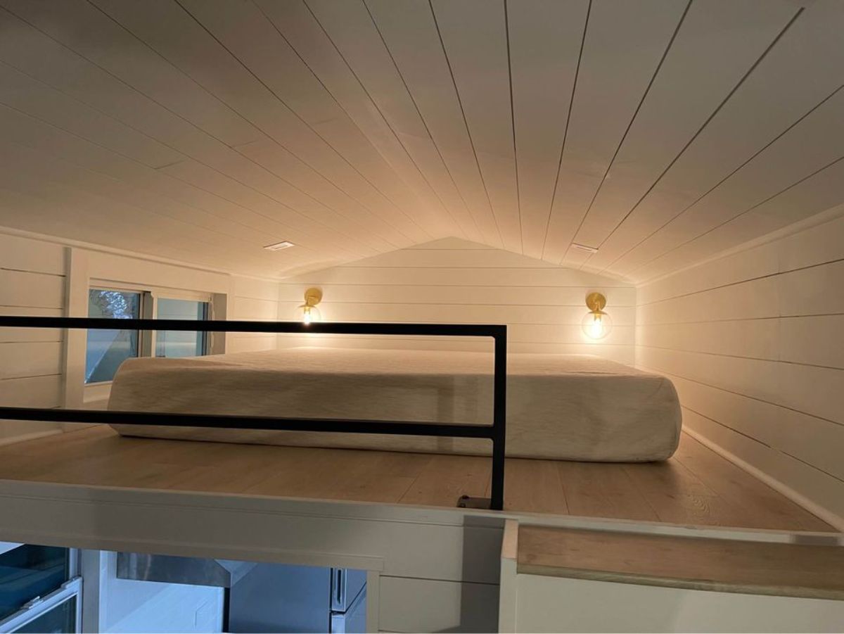 loft with lights against back wall and mattress on light wood floor with black matte bars at front of loft