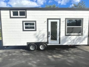 white tiny home with black trim and glass door on driveaway