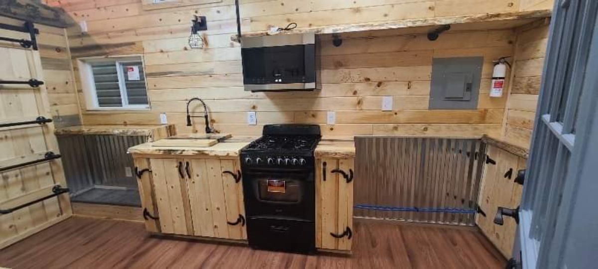 black stove in pine cabinet with open space at end with corrugated metal backing