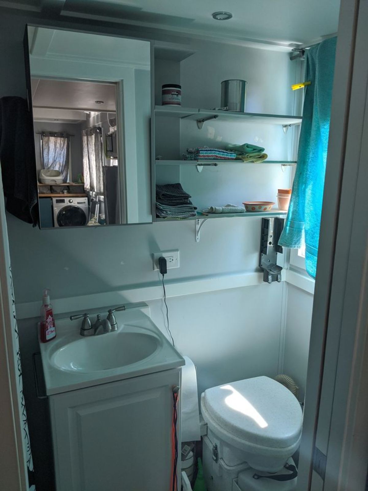 It has a compact bathroom with toilet, cabinet, sink and shower area