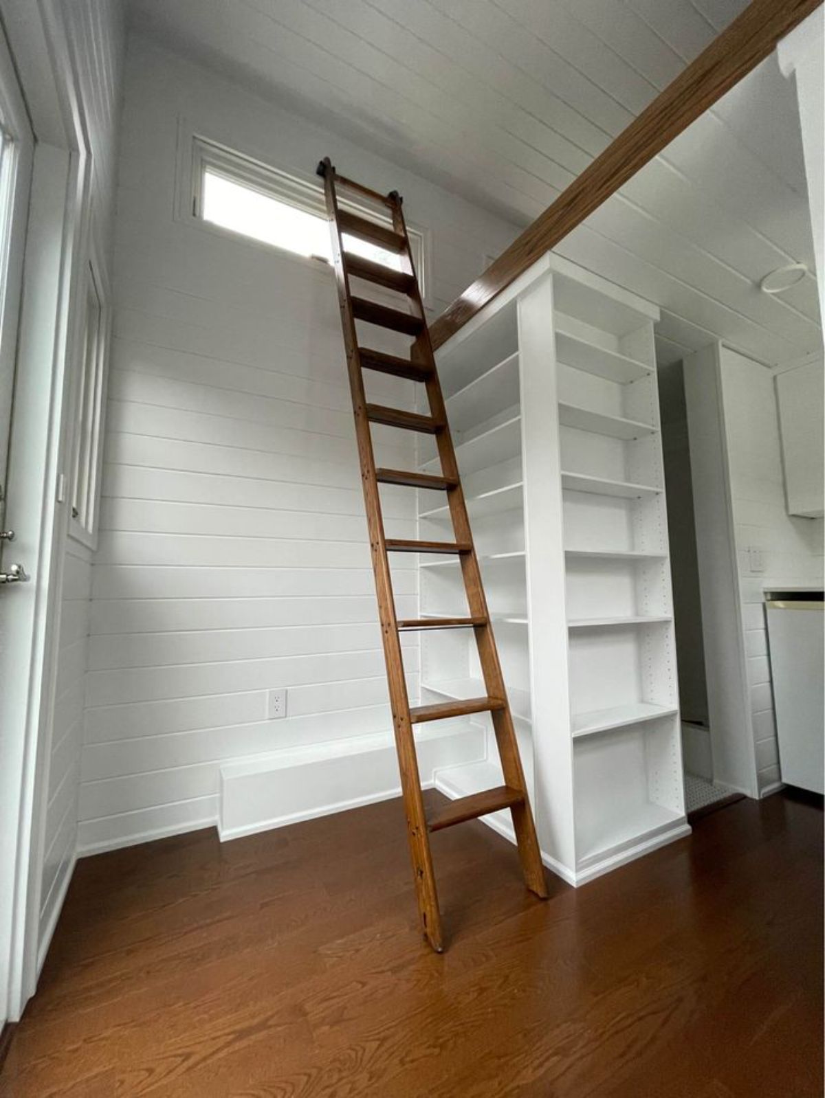 Wooden flooring with white interiors and a ladder to bedroom area of Tiny House on Wheels