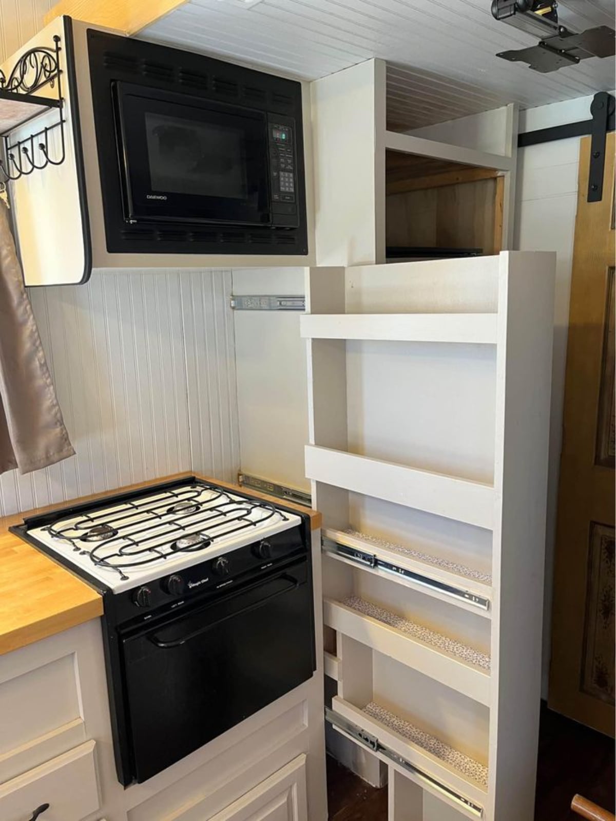 Kitchen of 152 sf Micro Tiny Home has a burner, a sink, an oven and slide out pantry rack beside the refrigerator and lots of storage cabinet