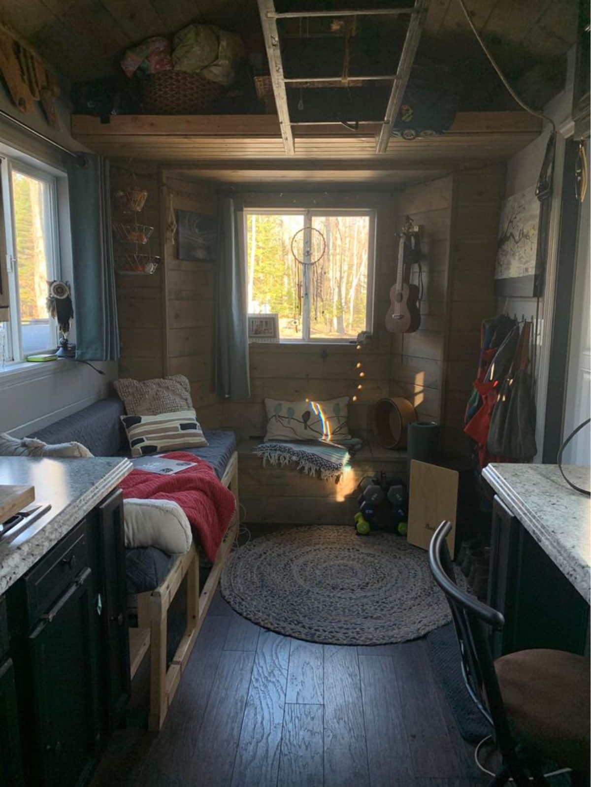 Living area of 180 sf Adorable Tiny House on Wheels has a large windows and L shaped sitting area