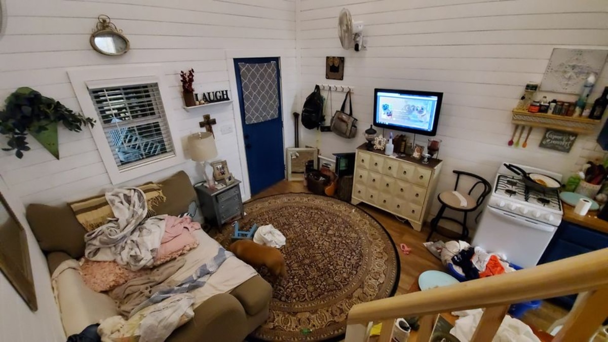 Living area of 24' Tiny House has a couch, television set, side table, lamp, a unit and other home appliances