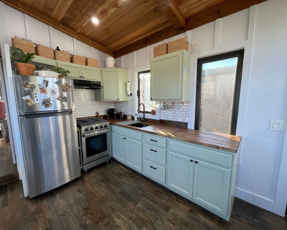 Kitchen area of 30’ Tiny House on Wheels  has counter table, sink, gas range, cabinets and refrigerator