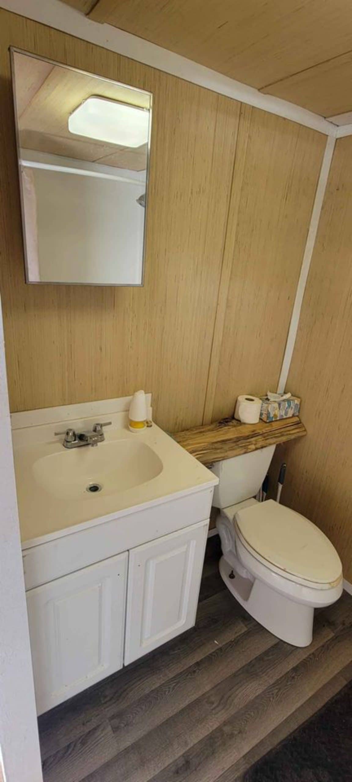 Standard toilet, sink with vanity and mirror is installed in bathroom of 28' Budget Friendly Tiny House
