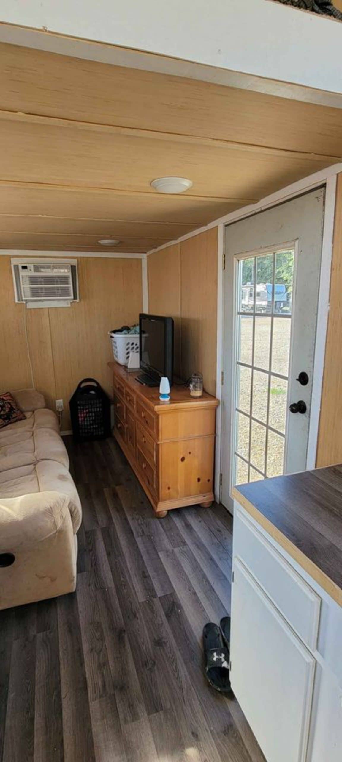 Opposite to couch there is wall unit and television set in the living area of 28' Budget Friendly Tiny House