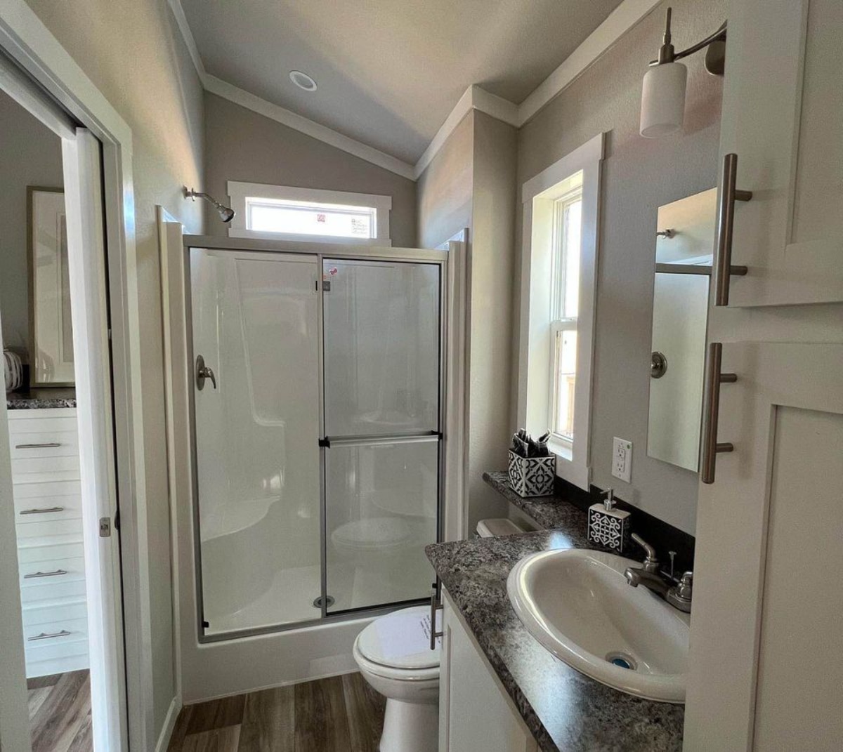 Stunning and stylish bathroom area of 32' Ranch Style Tiny Home has a toilet, separate shower area and sink with vanity & mirror
