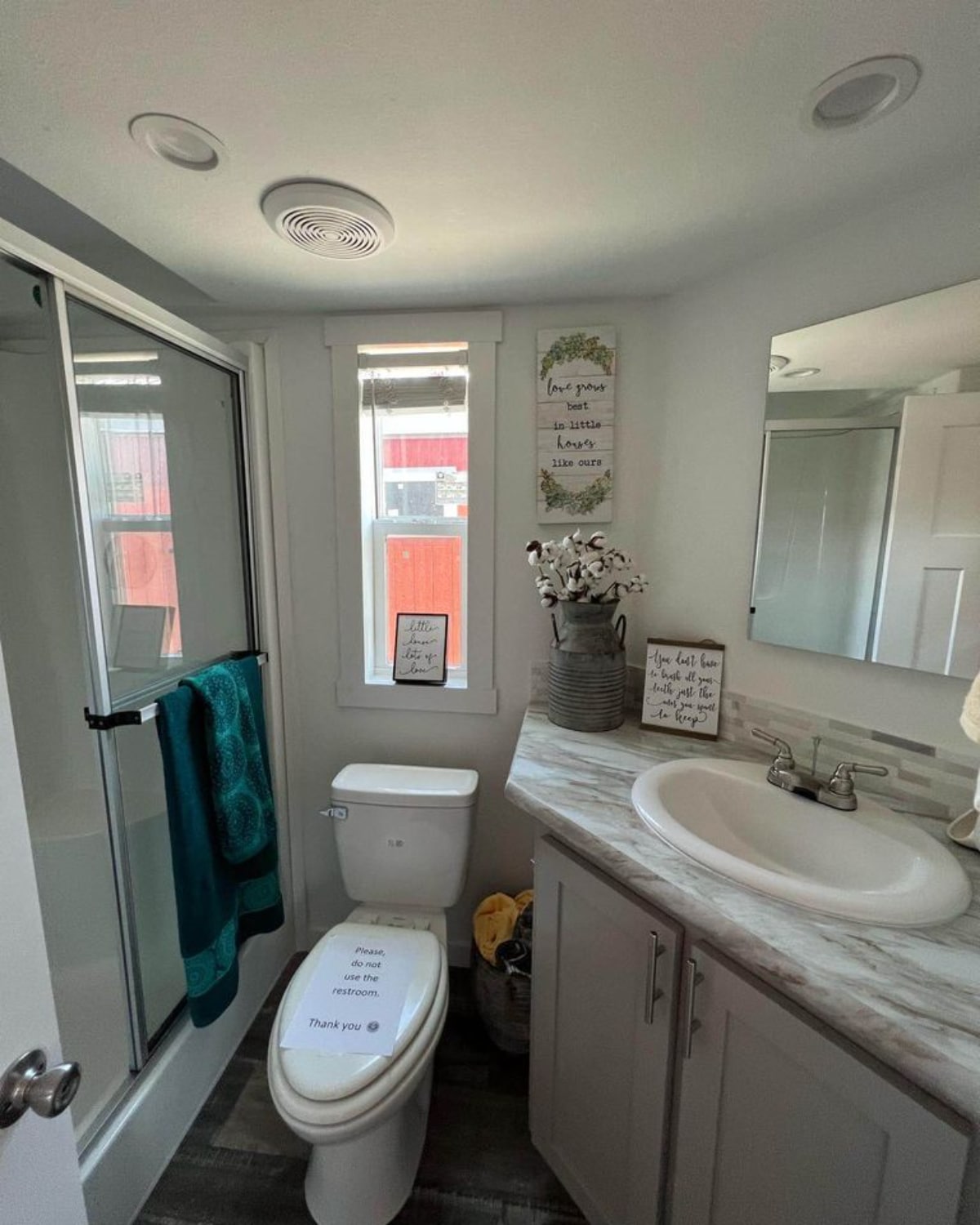 Beautifully organised bathroom of 399 sf Tiny House has a compact toilet, sink with vanity and mirror and separate shower area